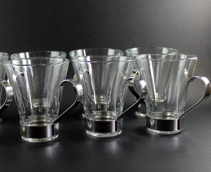 Set of clear glass mugs with metal handles on a black background