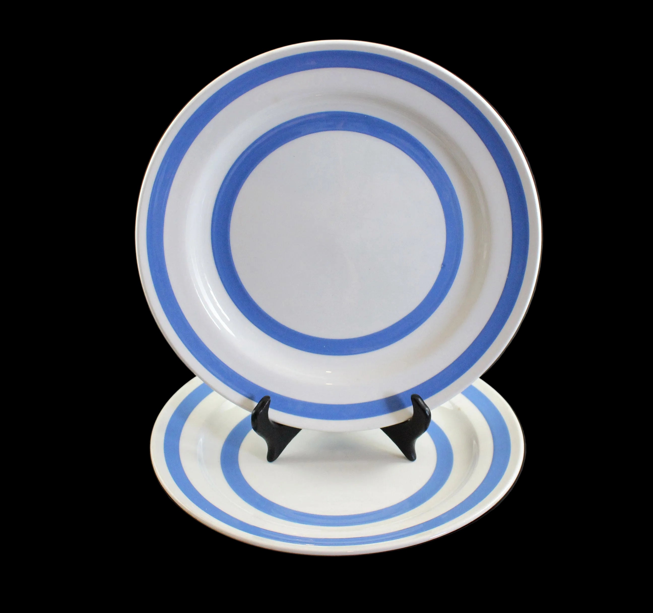 Two ceramic white plates with blue stripes on a black stand against a black background
