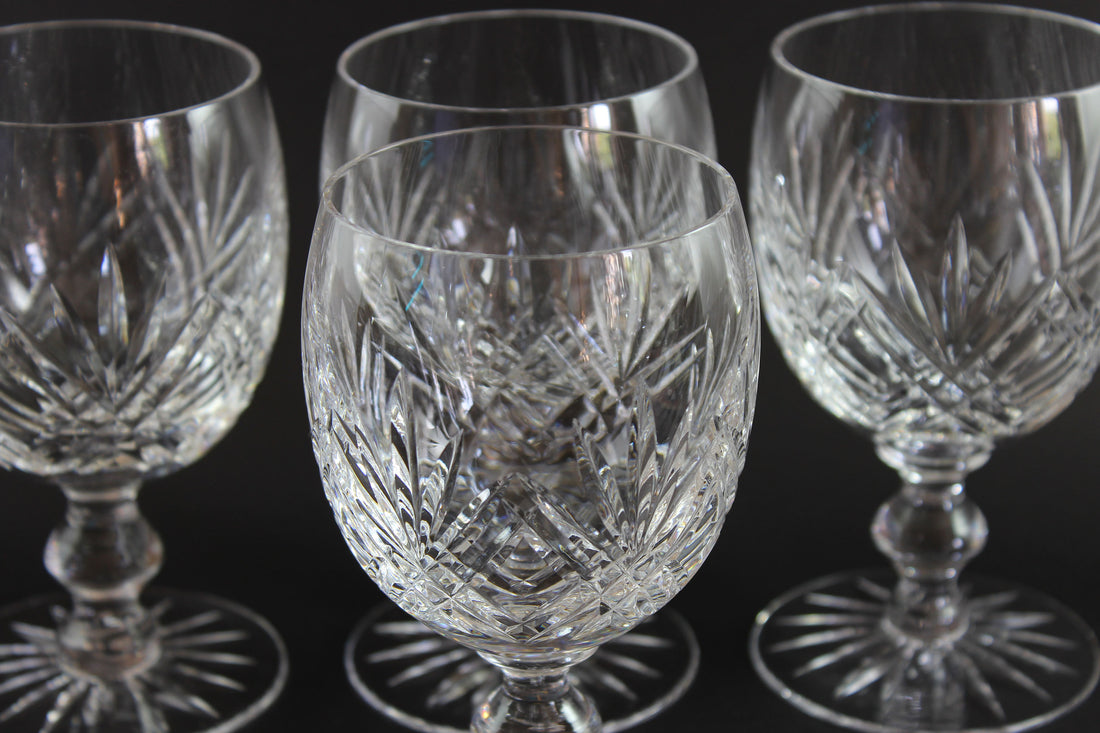 Set of four crystal wine glasses with intricate cut patterns on a black background