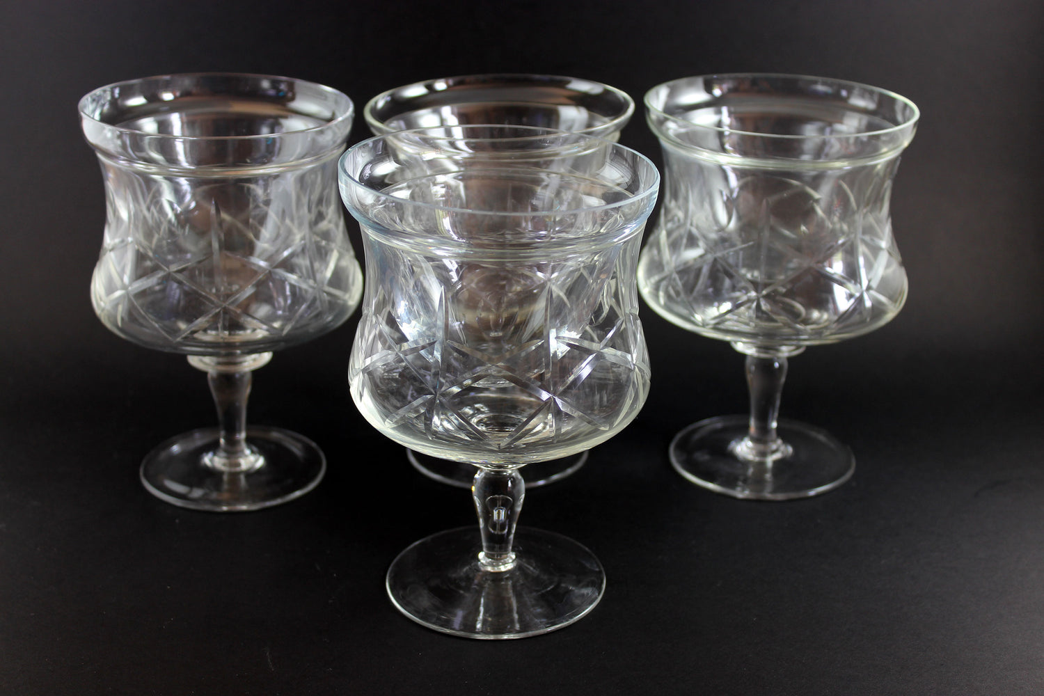 Four clear glass goblets with textured design on a black background