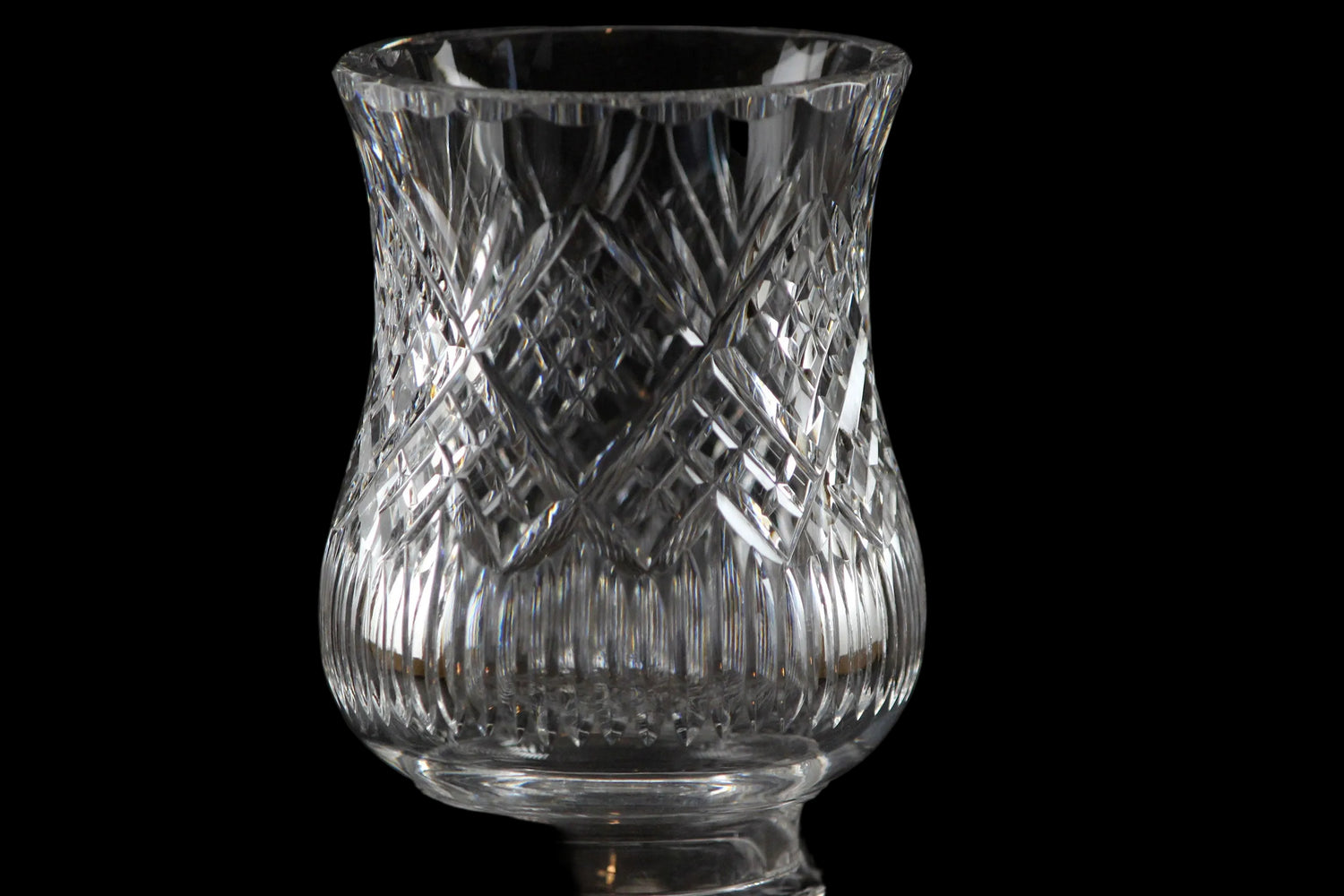 Clear glass hurricane lamp with intricate cut patterns on a black background