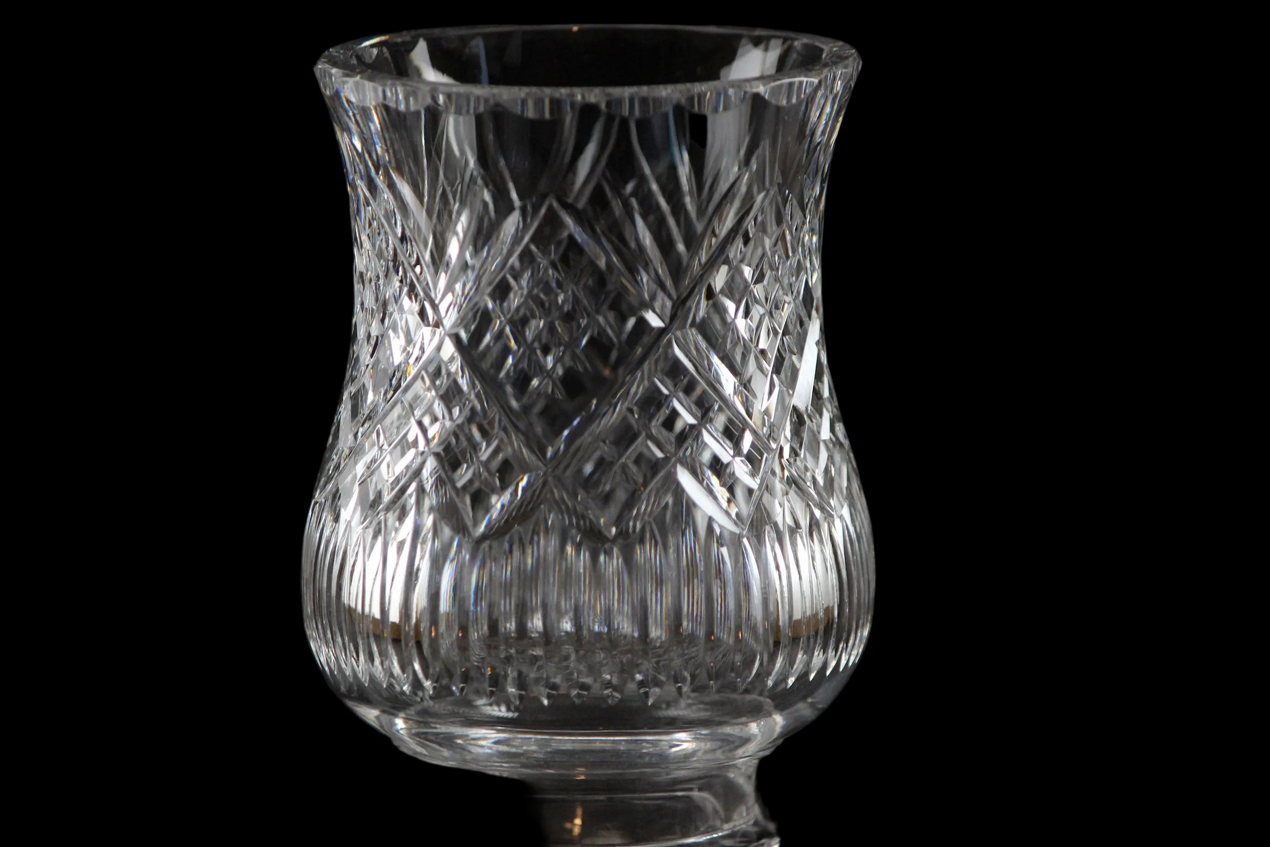 Clear glass hurricane lamp with intricate cut patterns on a black background