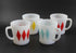 Set of four (4) white glass coffee mugs with a red, yellow, teal and red harlequin diamond pattern, set against a dark gray background.