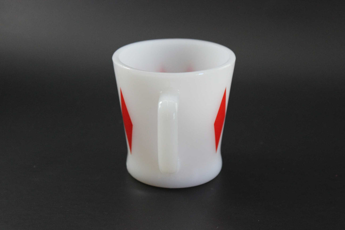 A white glass coffee mug with a red harlequin diamond pattern, set against a dark gray background.
