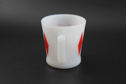 A white glass coffee mug with a red harlequin diamond pattern, set against a dark gray background.