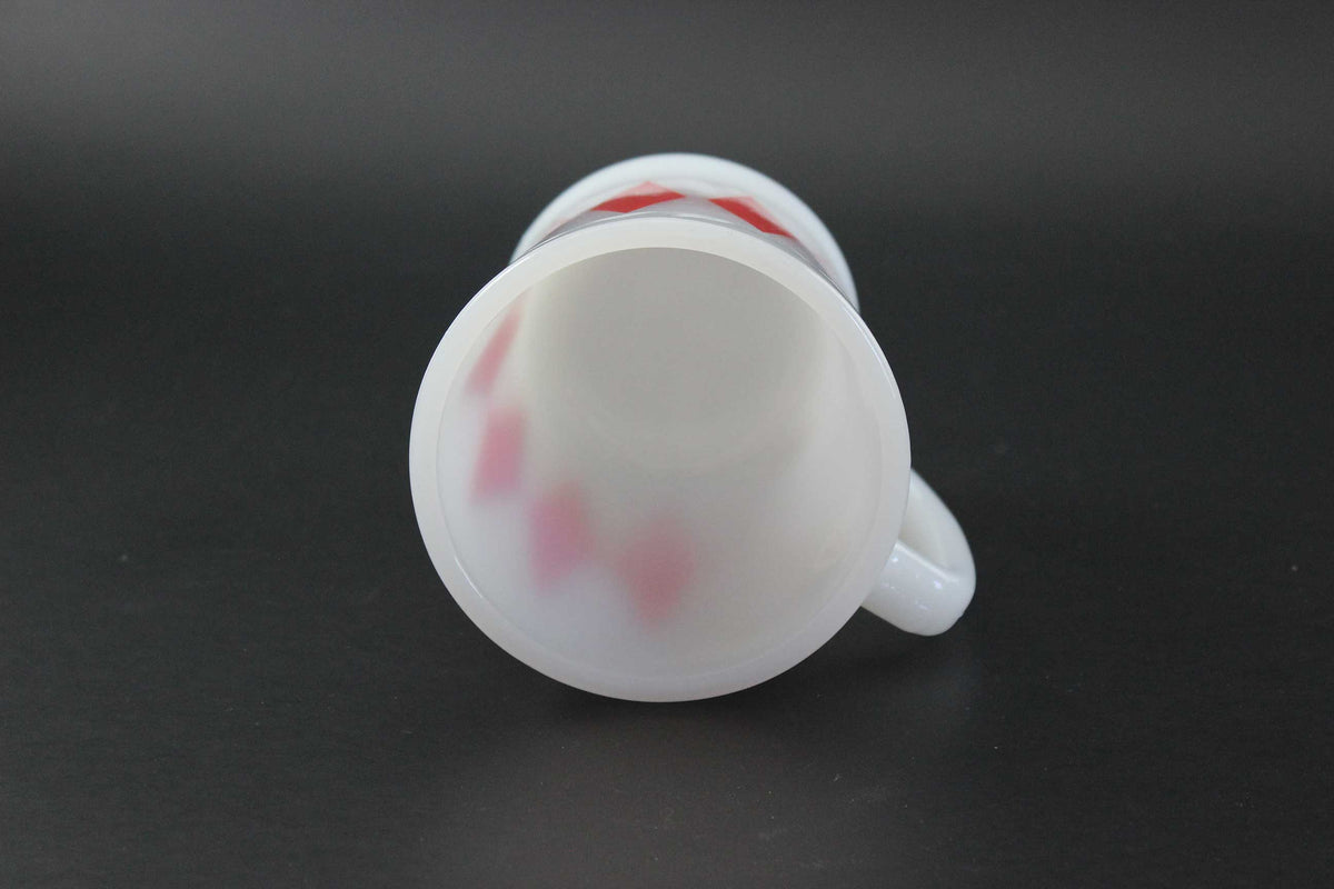 A white glass coffee mug with a red harlequin diamond pattern, set against a dark gray background.