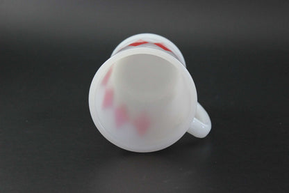 A white glass coffee mug with a red harlequin diamond pattern, set against a dark gray background.
