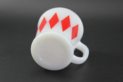 A white glass coffee mug with a red harlequin diamond pattern, set against a dark gray background.