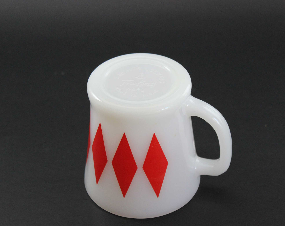 A white glass coffee mug with a red harlequin diamond pattern, set against a dark gray background.