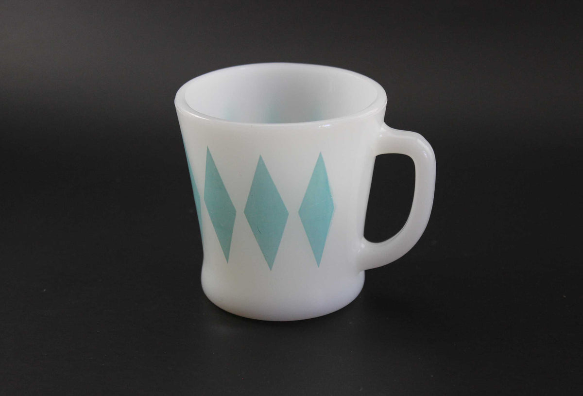 A white glass coffee mug with a teal harlequin diamond pattern, set against a dark gray background.