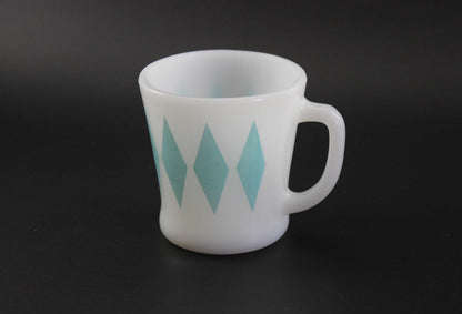 A white glass coffee mug with a teal harlequin diamond pattern, set against a dark gray background.