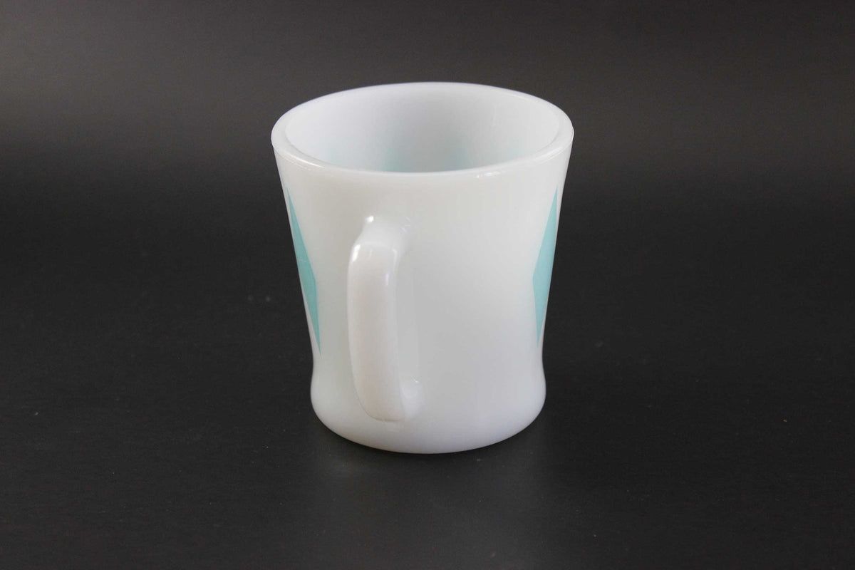 A white glass coffee mug with a teal harlequin diamond pattern, set against a dark gray background.