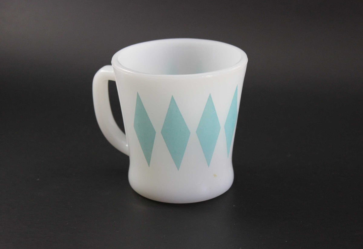 A white glass coffee mug with a teal harlequin diamond pattern, set against a dark gray background.