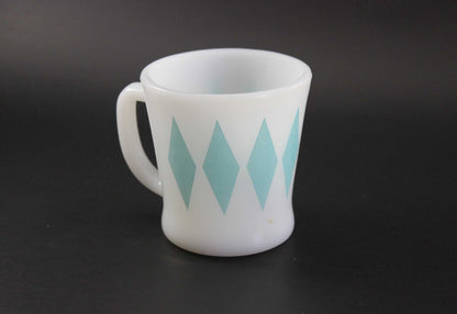 A white glass coffee mug with a teal harlequin diamond pattern, set against a dark gray background.