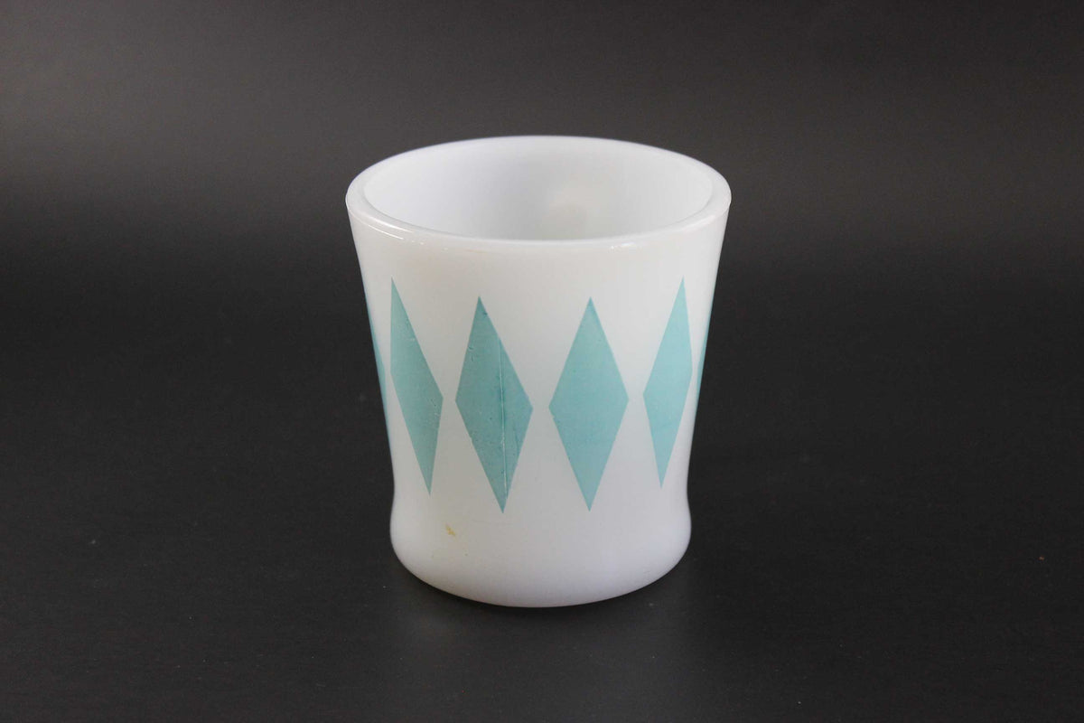 A white glass coffee mug with a teal harlequin diamond pattern, set against a dark gray background.