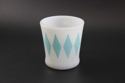 A white glass coffee mug with a teal harlequin diamond pattern, set against a dark gray background.