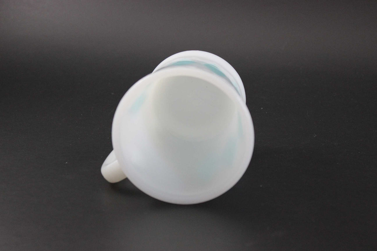 A white glass coffee mug with a teal harlequin diamond pattern, set against a dark gray background.