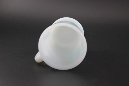 A white glass coffee mug with a teal harlequin diamond pattern, set against a dark gray background.
