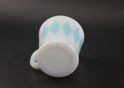 A white glass coffee mug with a teal harlequin diamond pattern, set against a dark gray background.
