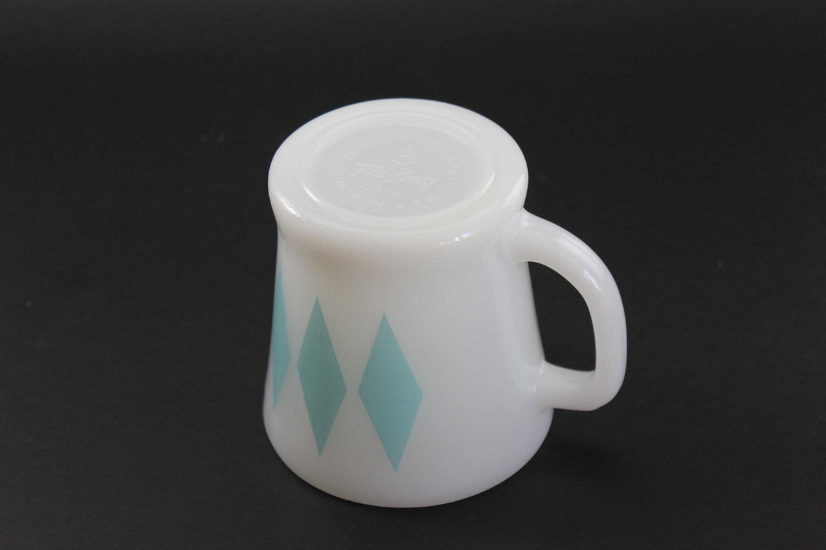 A white glass coffee mug with a teal harlequin diamond pattern, set against a dark gray background.
