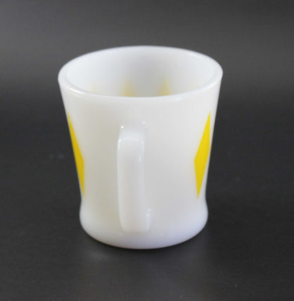 A white glass coffee mug with a yellow harlequin diamond pattern, set against a dark gray background.