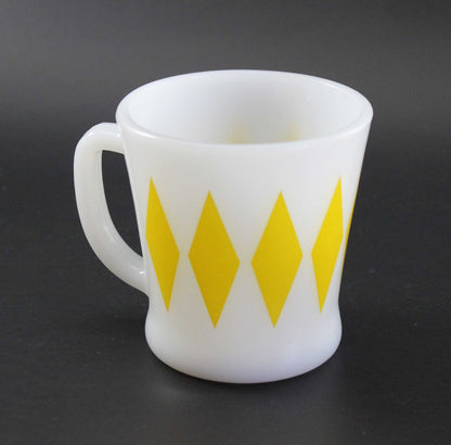 A white glass coffee mug with a yellow harlequin diamond pattern, set against a dark gray background.