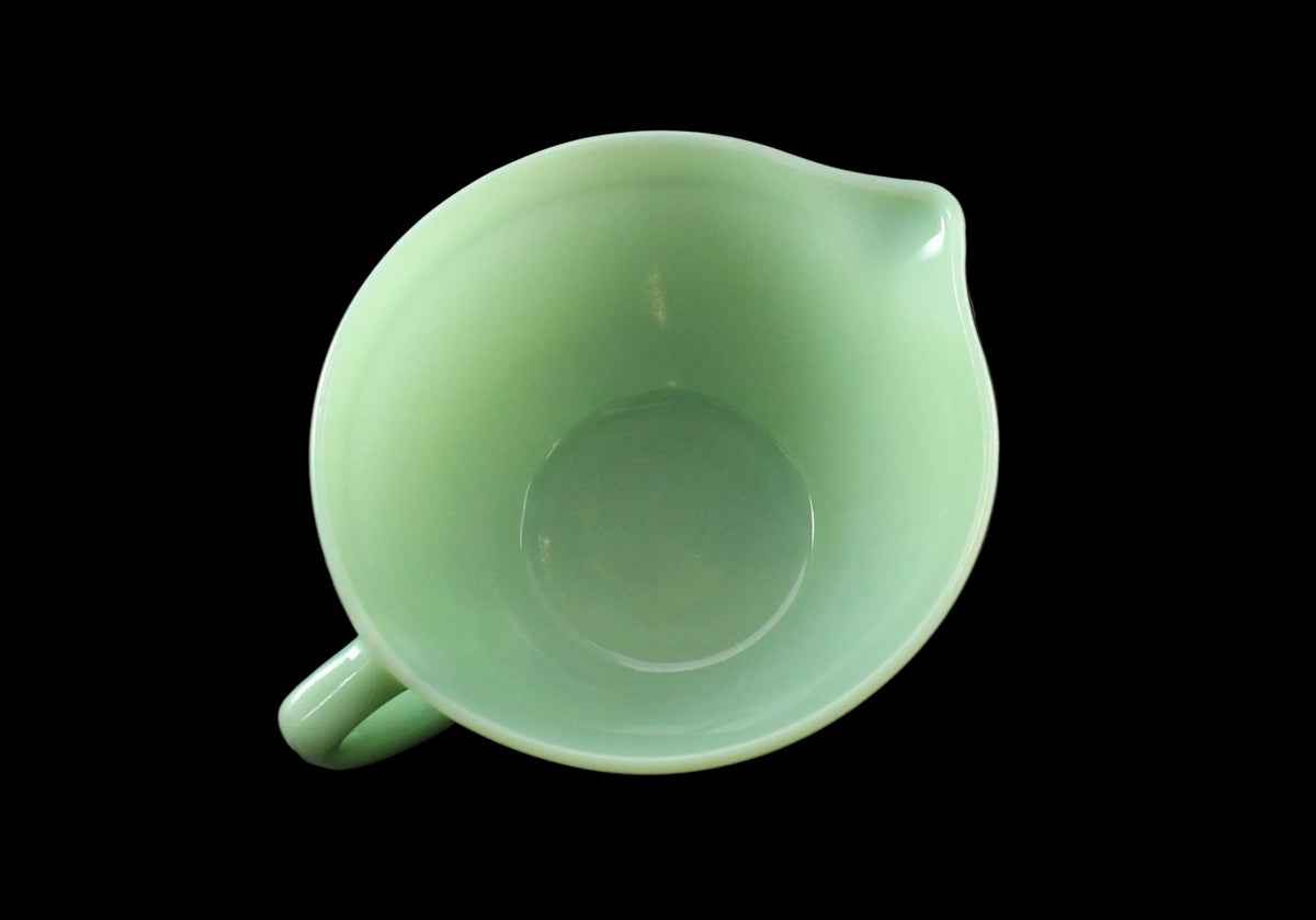 A vintage light green glass pitcher with a pouring spout and handle, photographed on a dark gray background.