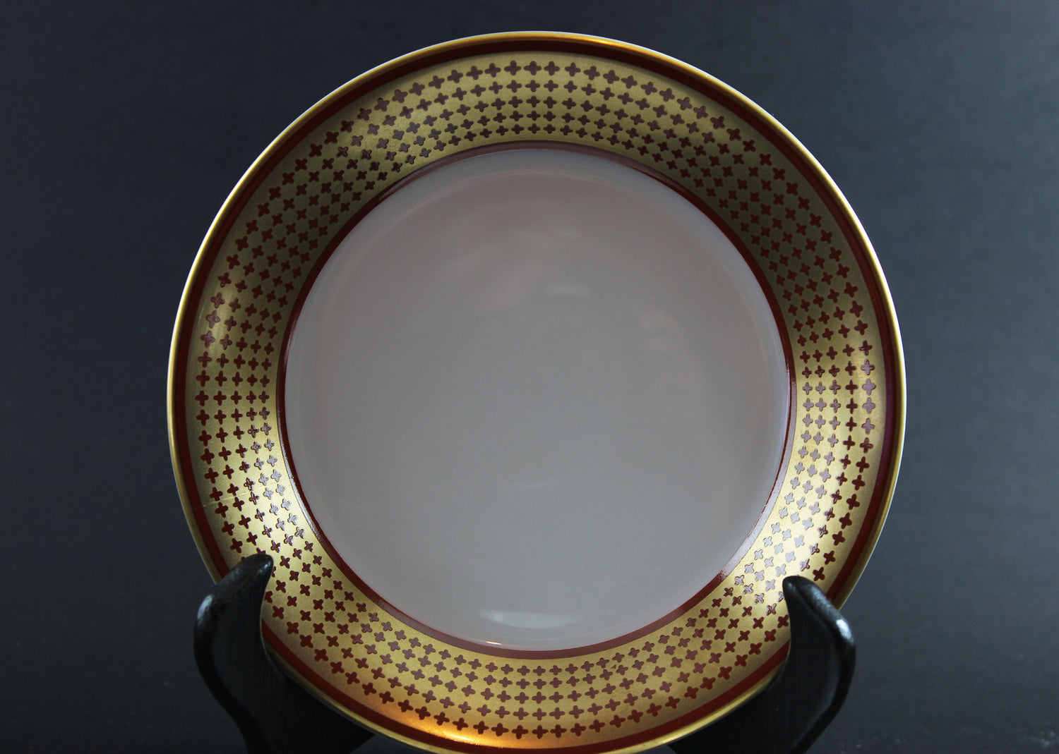 White bowl with gold decorative rim on a black stand against a dark background