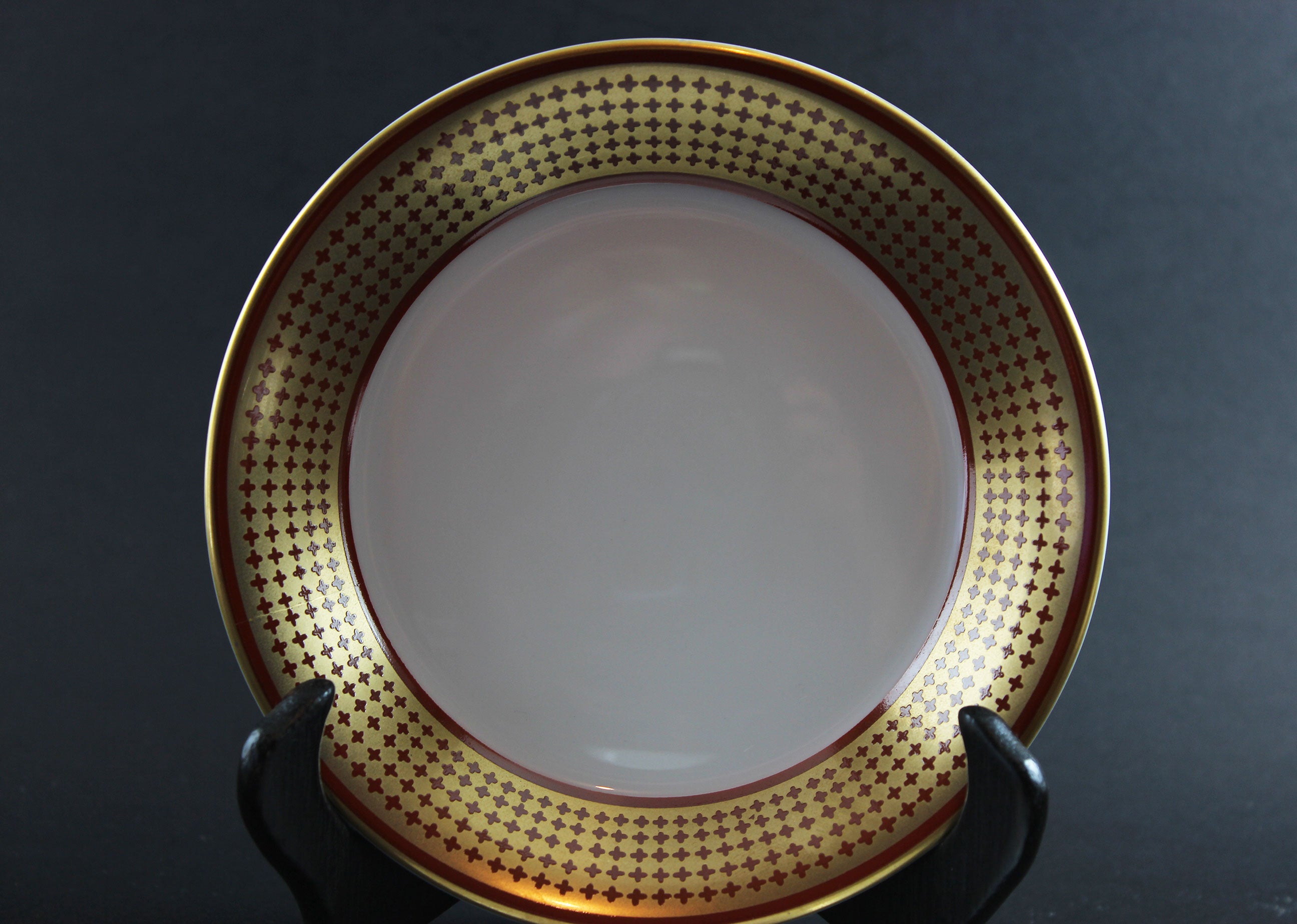 White bowl with gold decorative rim on a black stand against a dark background
