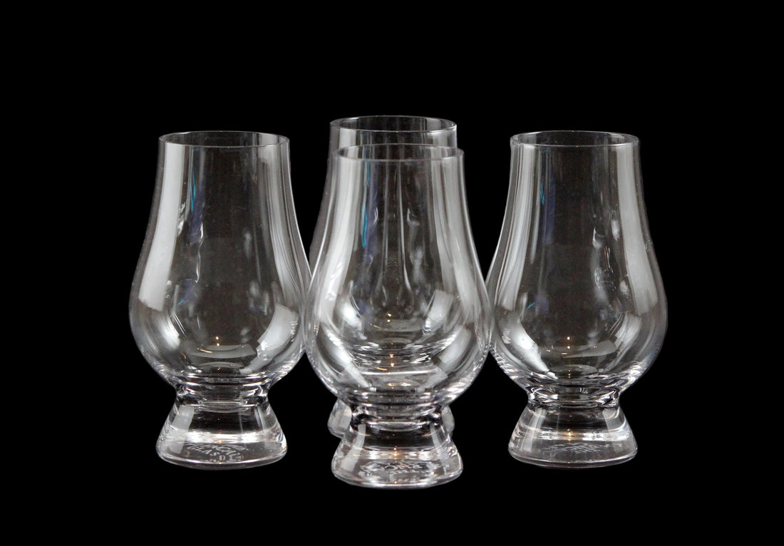 Four clear glass whisky glasses on a black background