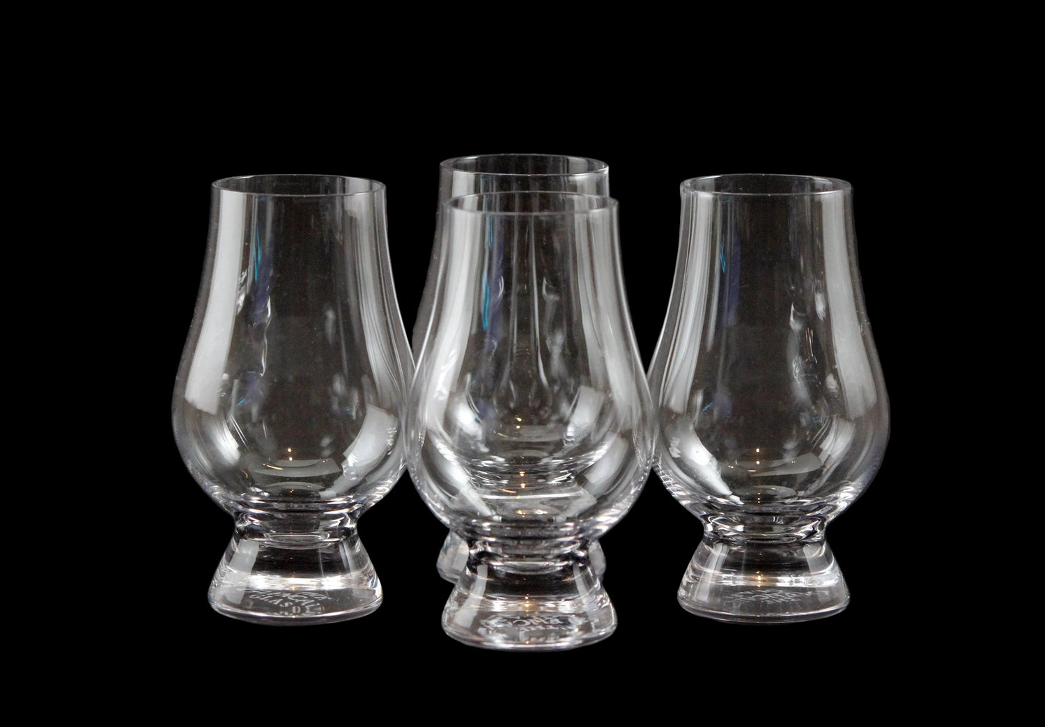 Four clear glass whisky glasses on a black background