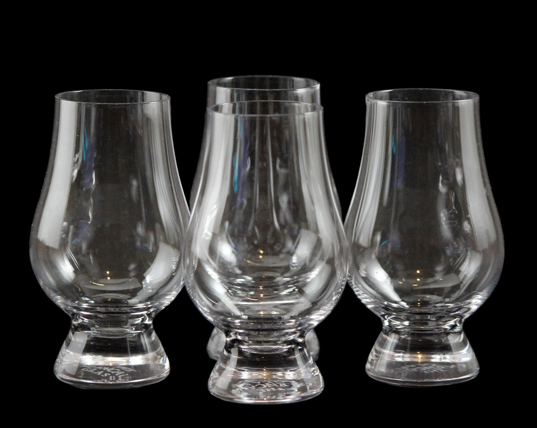 Four clear glass whisky glasses on a black background