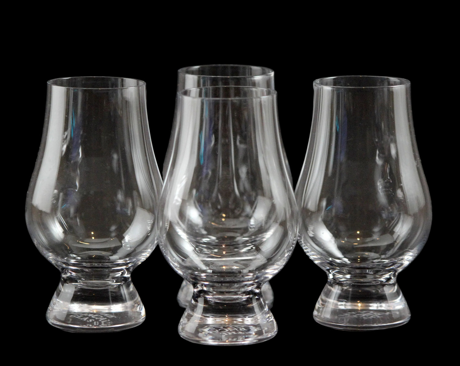 Four clear glass whisky glasses on a black background