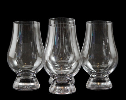 Four clear glass whisky glasses on a black background
