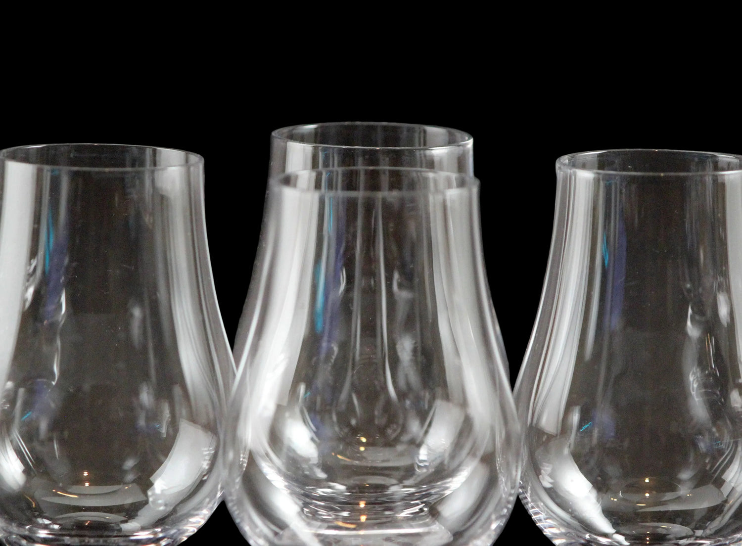Four clear glass whisky glasses on a black background