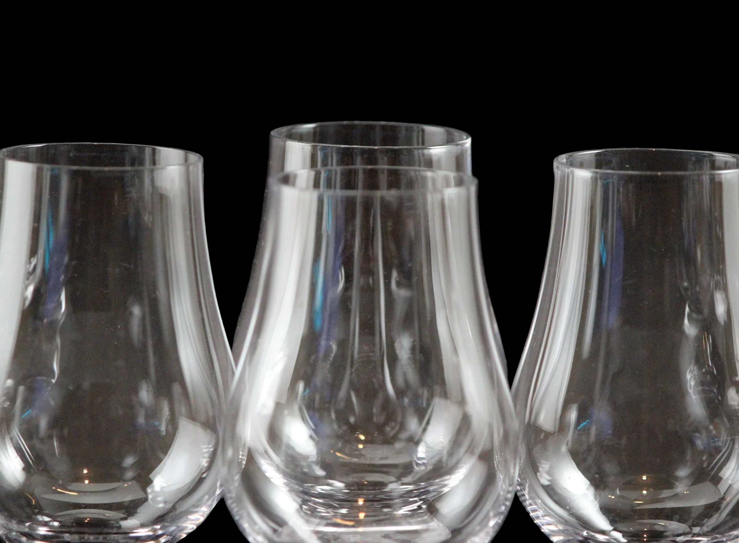 Four clear glass whisky glasses on a black background