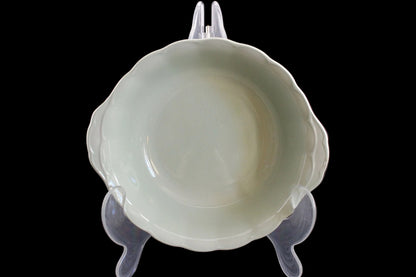 Light green ceramic bowl on a clear stand against a dark background