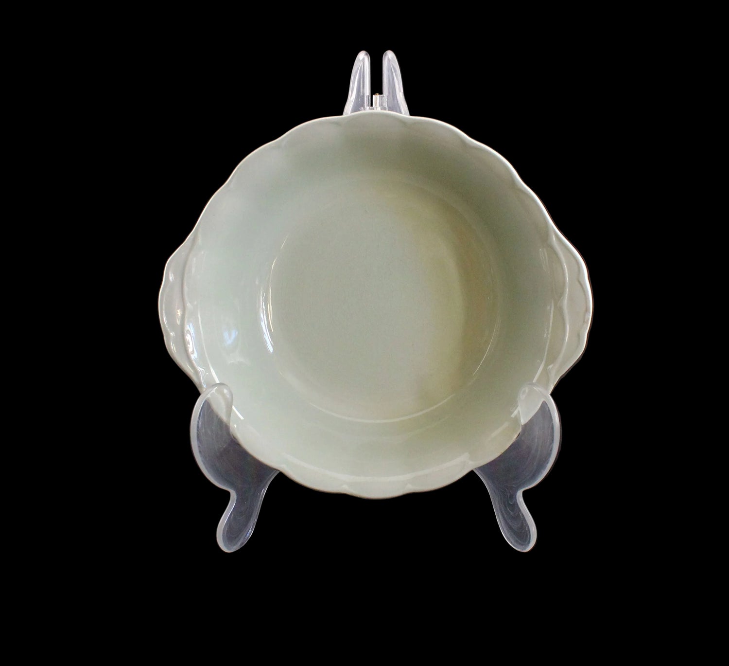 Light green ceramic bowl on a clear stand against a dark background