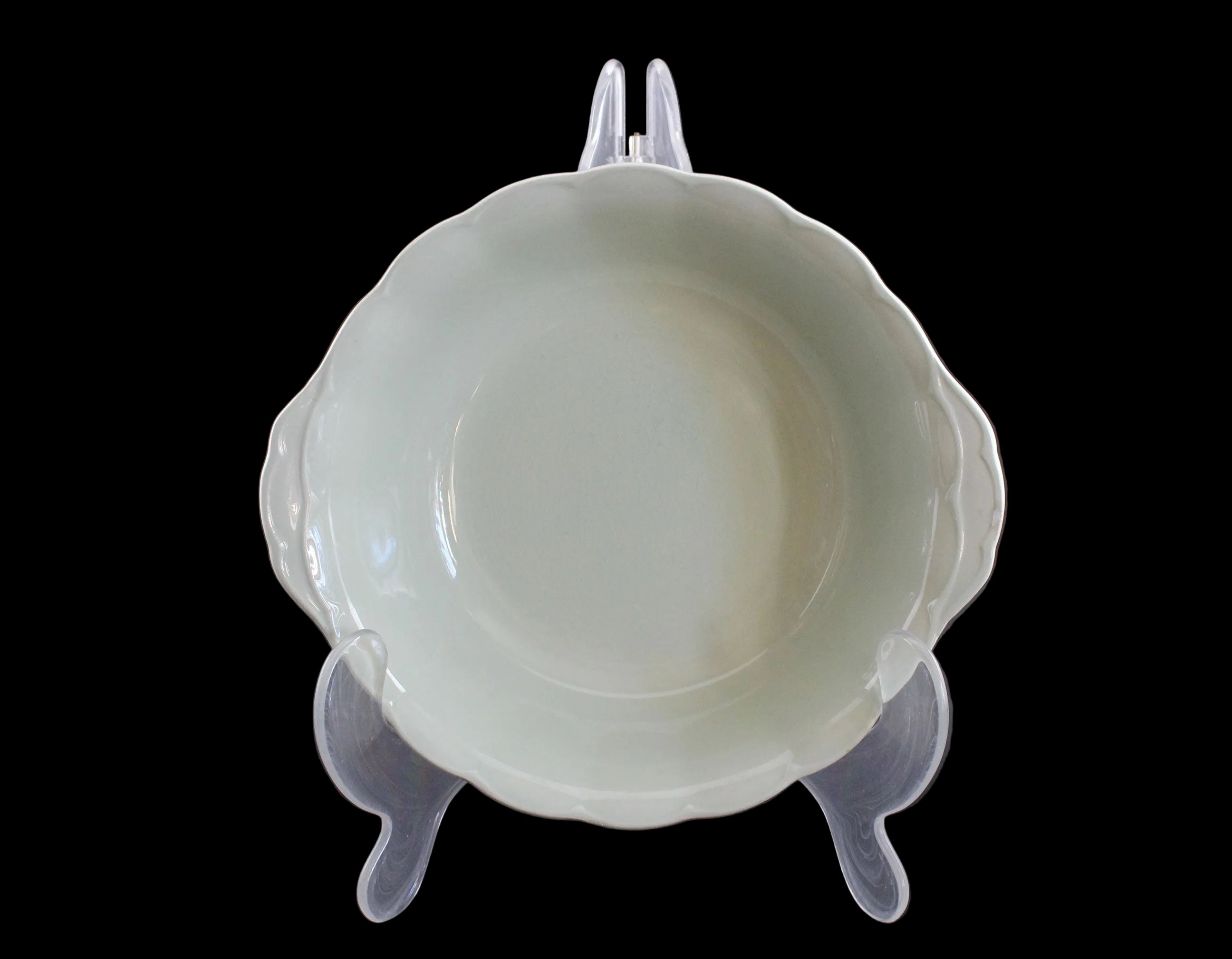 Light green ceramic bowl on a clear stand against a dark background