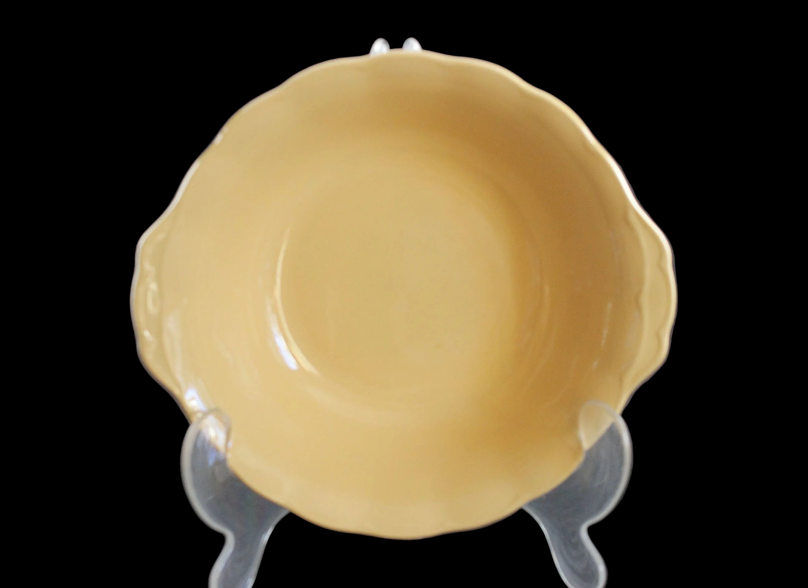 Yellow ceramic bowl on a clear stand against a dark background