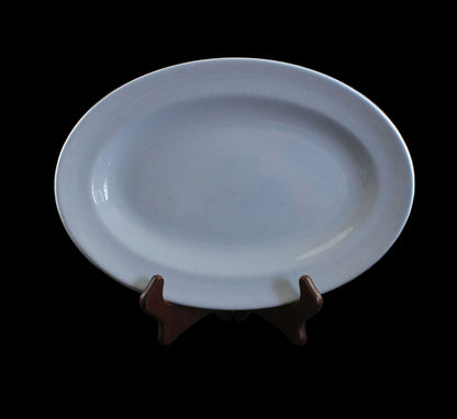 An oval blue ceramic serving platter displayed on a small dark brown wooden stand against a dark gray studio background.