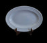 An oval blue ceramic serving platter displayed on a small dark brown wooden stand against a dark gray studio background.
