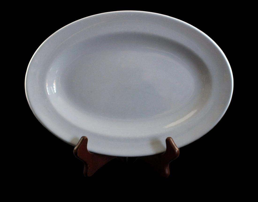 A blue ceramic oval platter displayed on a small dark brown wooden stand against a dark gray background.