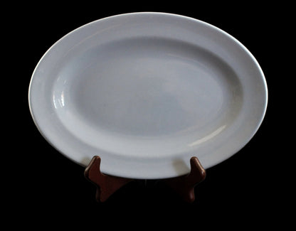 A blue ceramic oval platter displayed on a small dark brown wooden stand against a dark gray background.