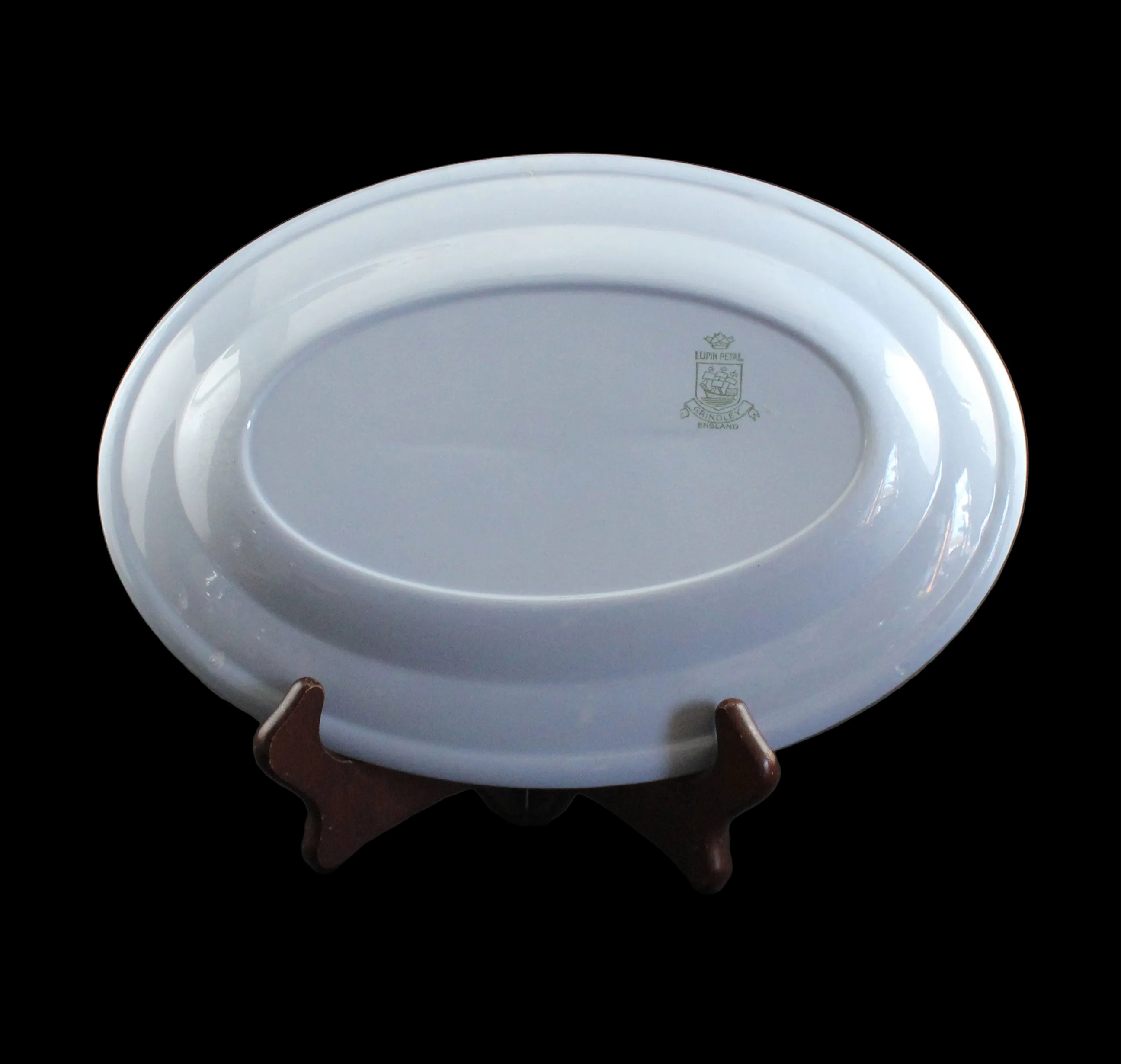 An oval blue ceramic plate with a small green crest emblem, displayed on a dark wooden stand against a dark gray background.