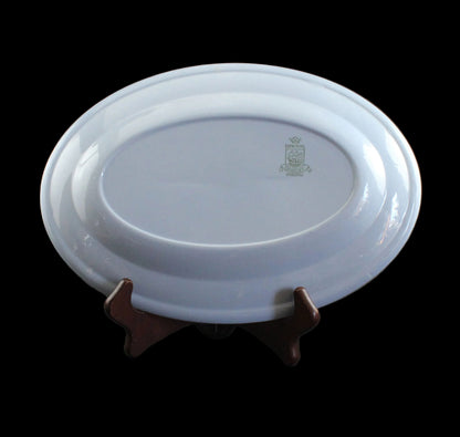 An oval blue ceramic plate with a small green crest emblem, displayed on a dark wooden stand against a dark gray background.