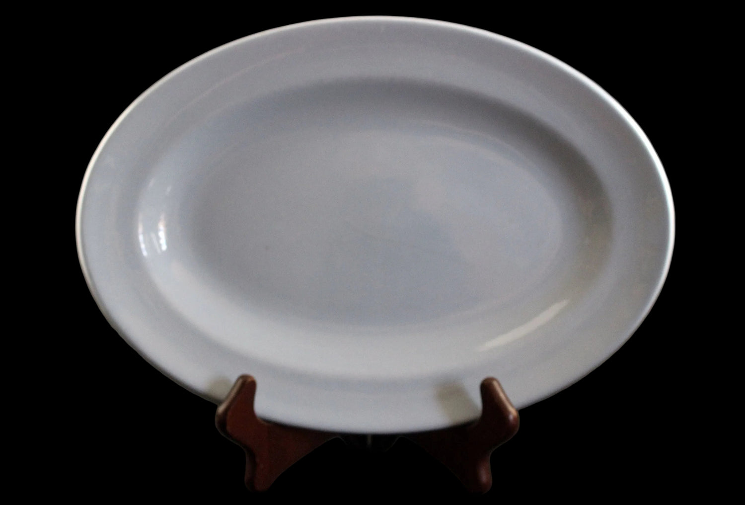 A light blue ceramic oval platter with a glossy finish, displayed on a small dark brown wooden stand against a dark gray background.