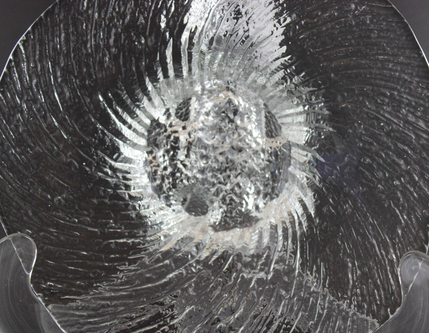 Clear glass footed bowl with textured surface on a dark background