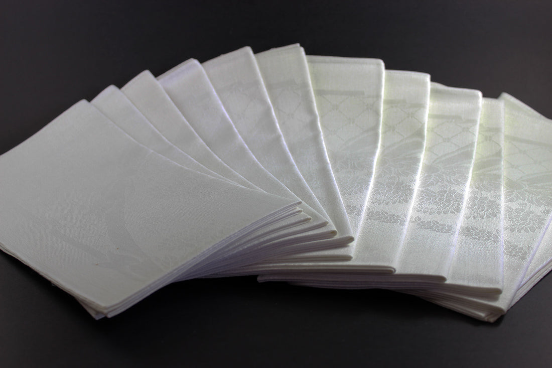 Twelve white damask Irish linen napkins on black background.