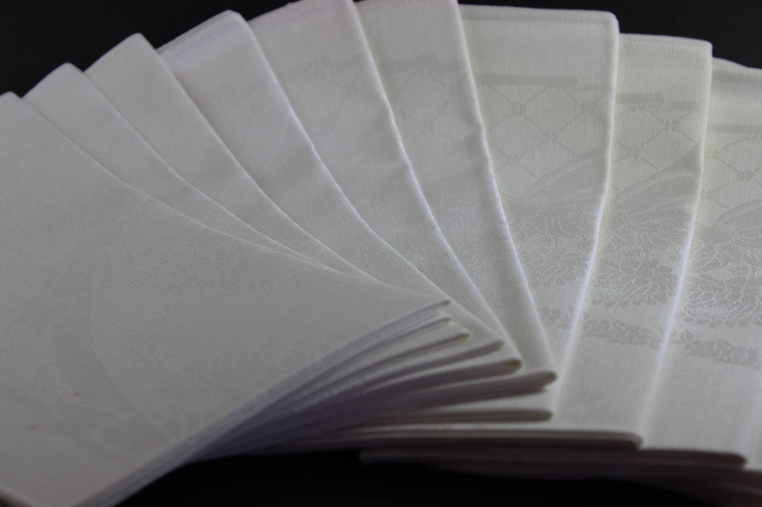 Twelve white damask Irish linen napkins on black background.